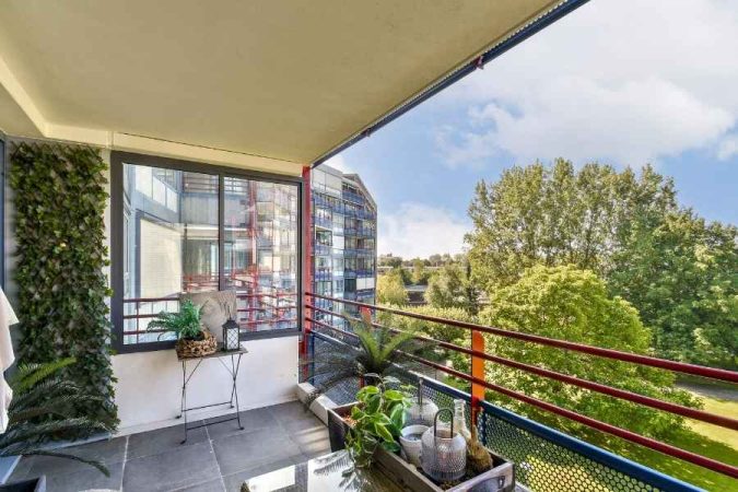Un grand balcon moderne avec un mur végétal, des plantes en pot et une vue dégagée sur la ville et les arbres pour l'aménagement de son balcon.
