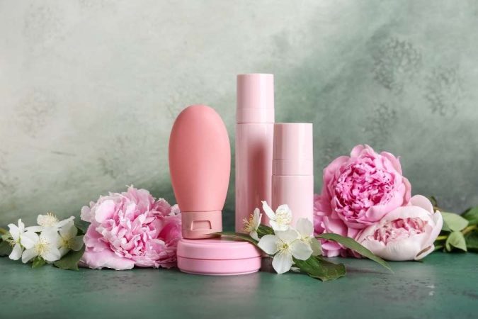Flacons roses de cosmétiques bio entourés de fleurs de pivoine et de jasmin.
