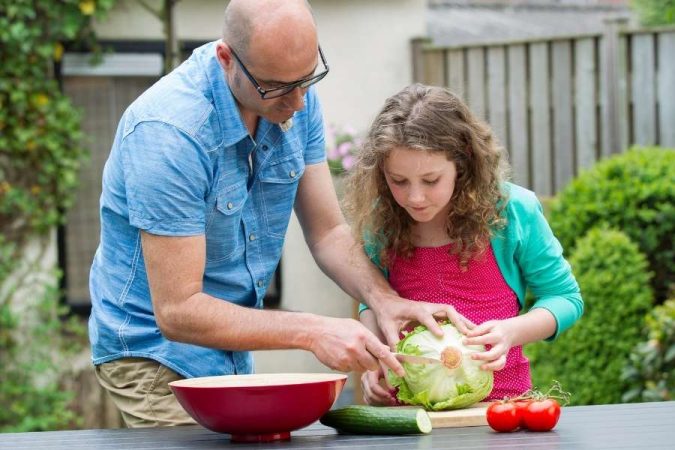 Un père et sa fille découpent de la salade pour la préparation des repas en plein air.