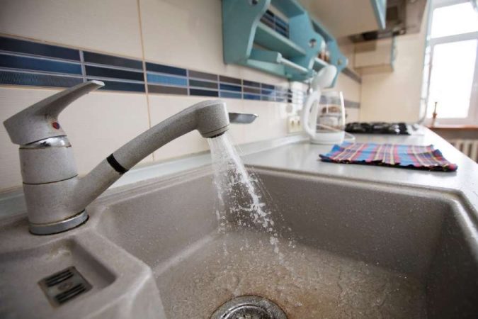 Un mitigeur de cuisine ancien coule au-dessus d'un évier en pierre, illustrant une installation où la pression de l'eau baisse de manière anormale.